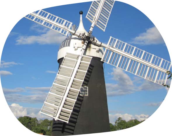 A photo of Tuxford Windmill, a dark building with large white sails, against a blue sky.